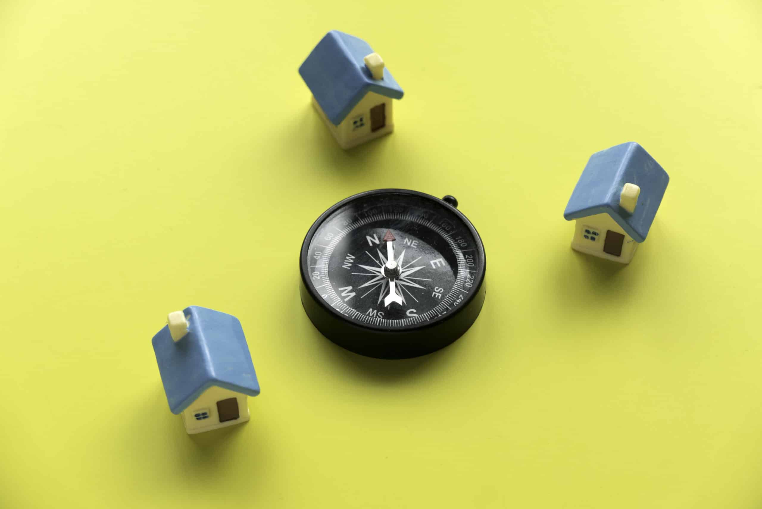 Miniature house and a compass over a yellow background.